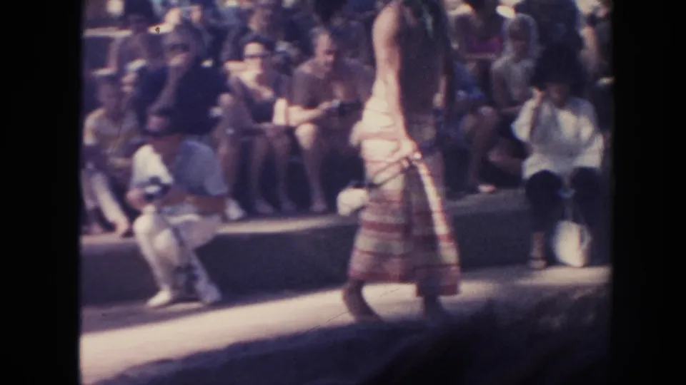 A side view shows the barefoot performer moving past the coal area as the outdoor audience remains seated nearby.