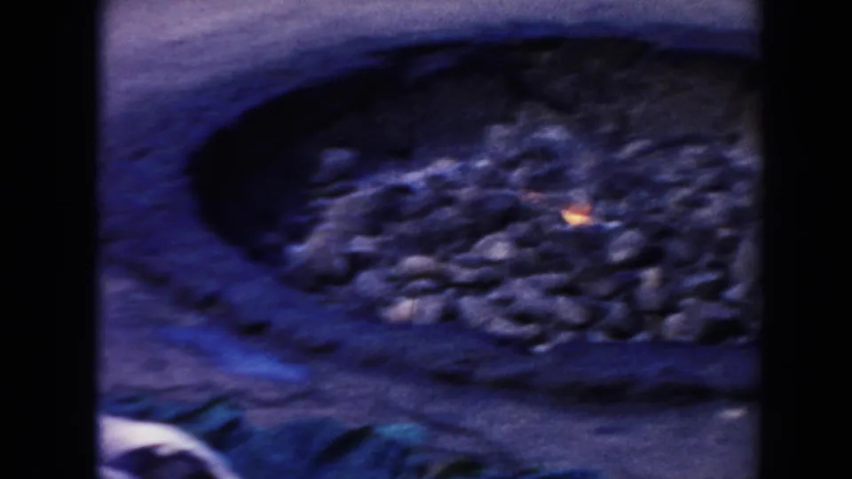 1961 Hawaii 8mm frame showing a stone-lined outdoor fire pit with a small flame near the animal carcass.