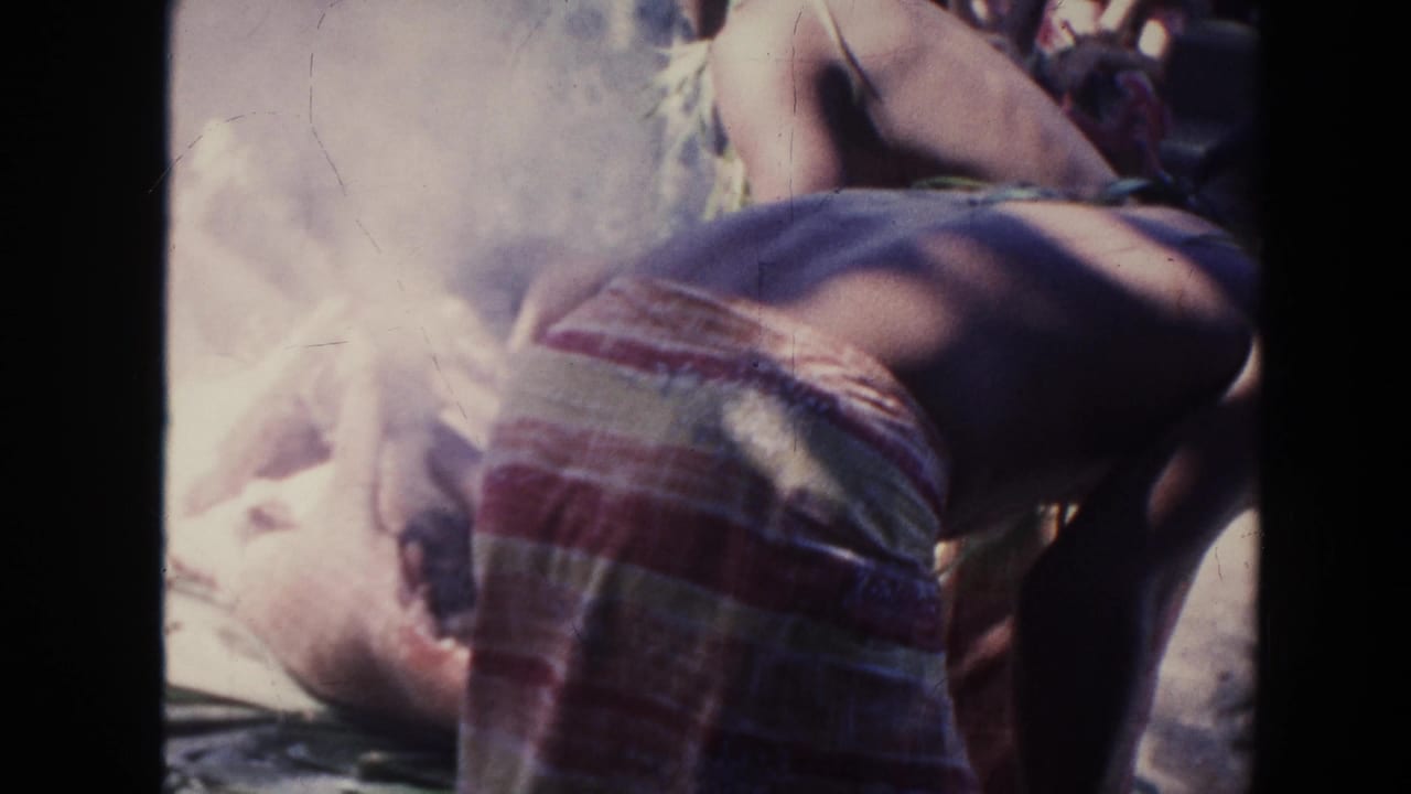 Shirtless person bends near a smoky fire while another figure lies or sits low nearby.