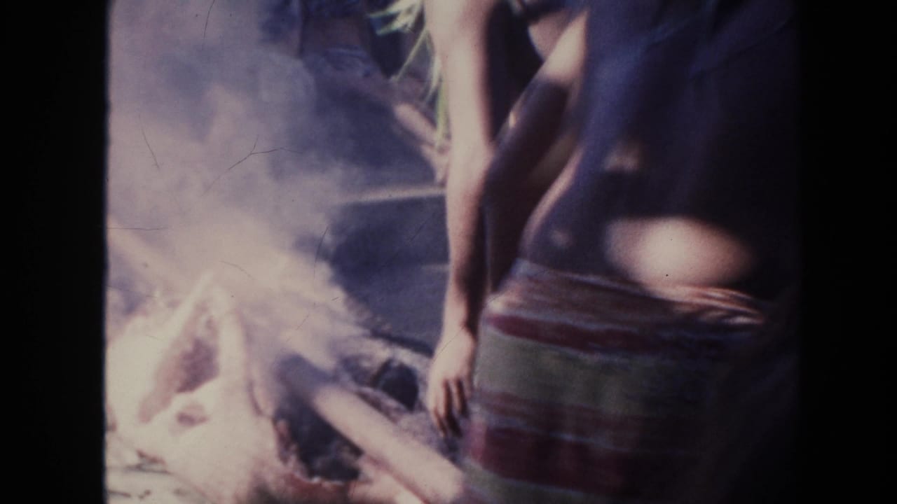 1961 Hawaii home-movie frame with a person in a striped wrap standing near smoke as onlookers sit behind.