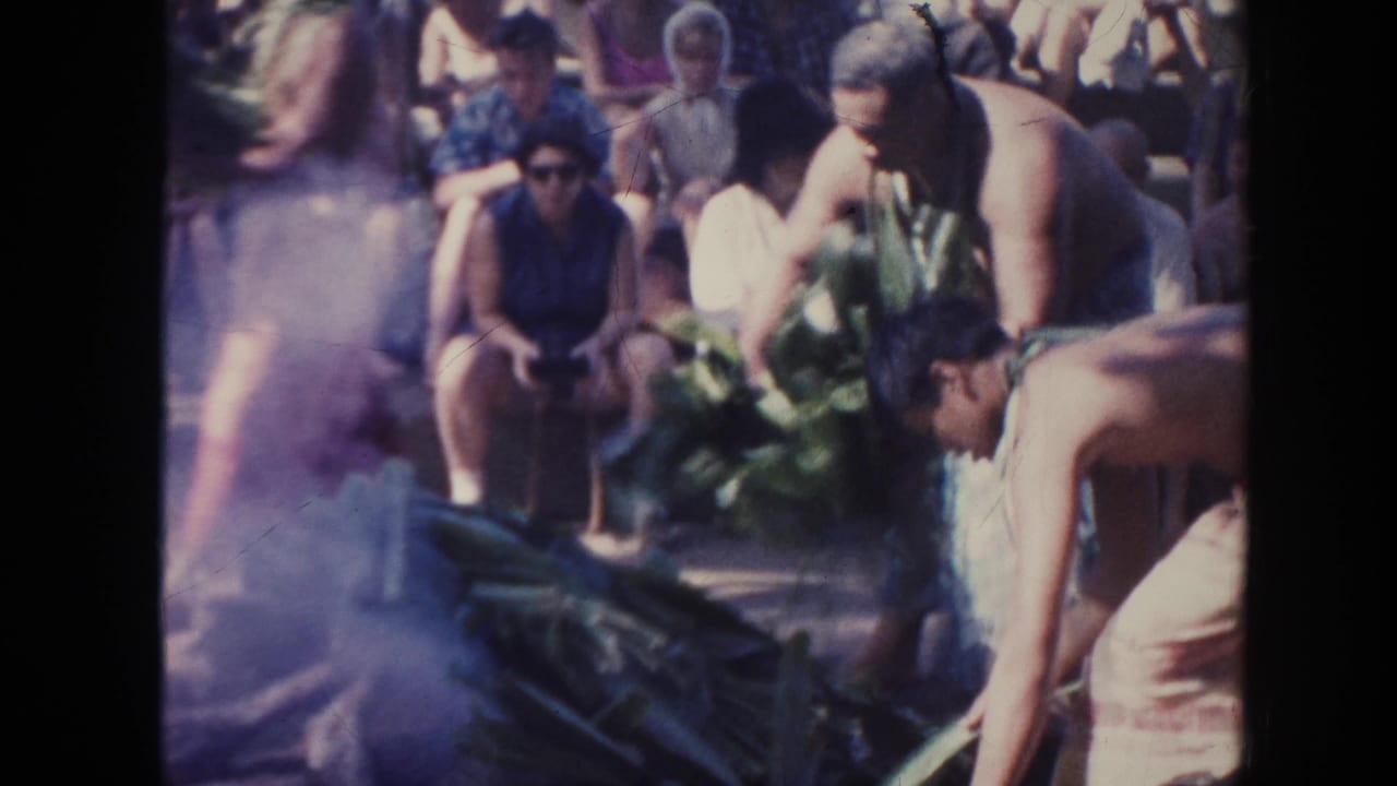 Men tend large leaves over smoke while spectators sit nearby.