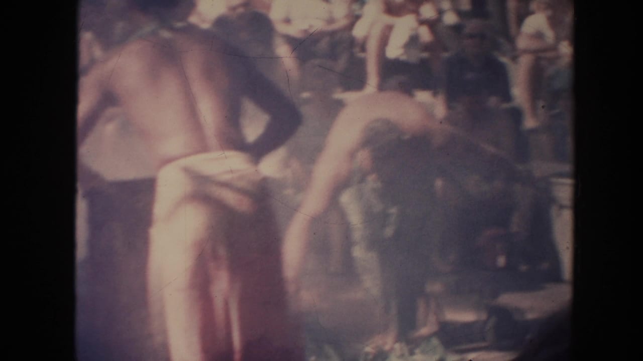 Two shirtless performers bend near mats in front of a seated crowd.