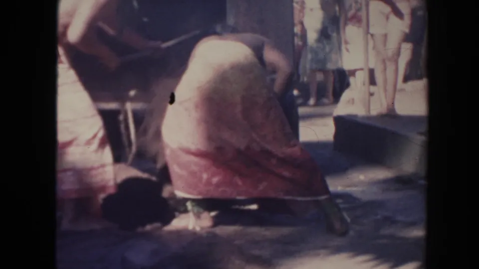 1961 Hawaii 8mm frame showing a worker crouched low near shovels and a container, with bystanders behind him.