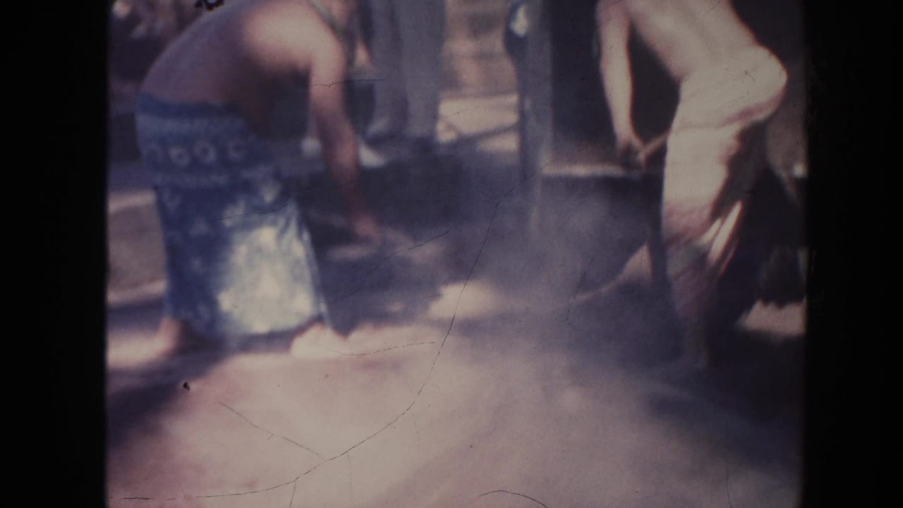 Two shirtless men bend over shovels in a dusty outdoor work area.