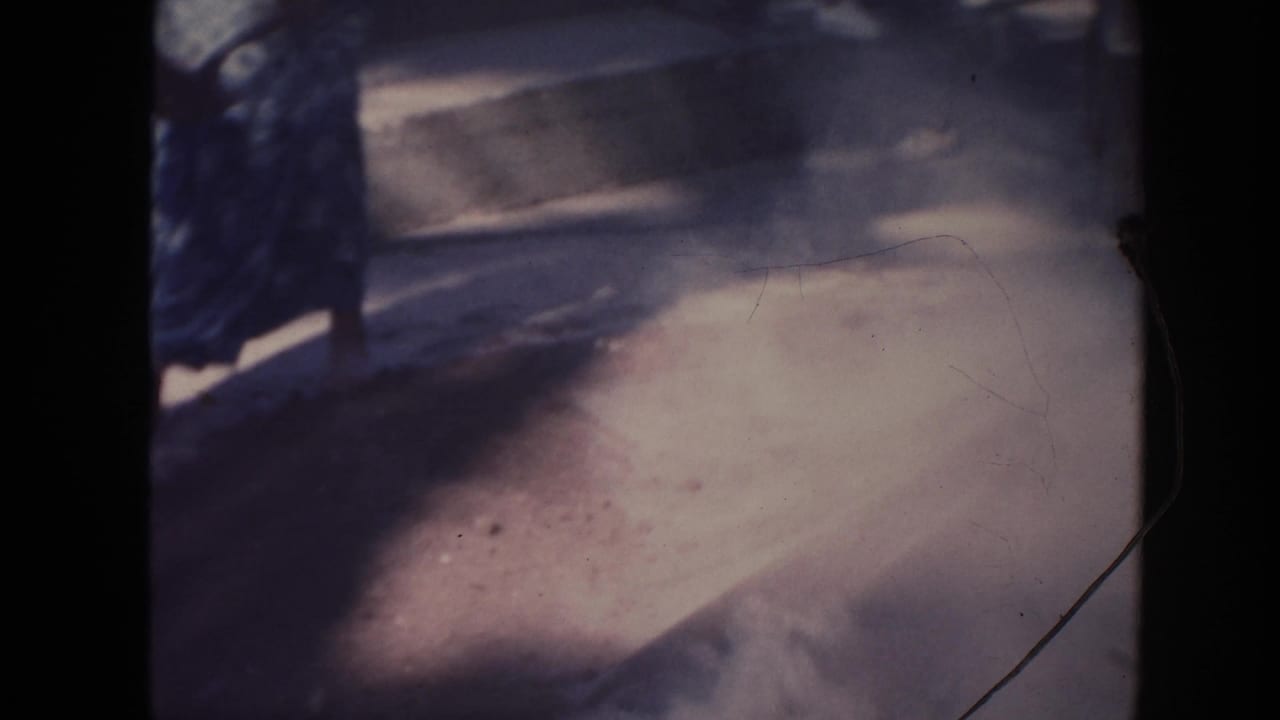 1961 Hawaii 8mm frame with sunlit dust or sand near a blue metal container and partial figures at the frame edge.