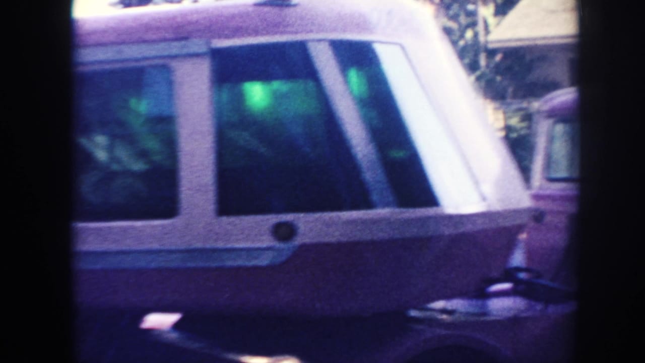 Pink and white bus partly obscured by a passing vehicle and dark film-frame borders.
