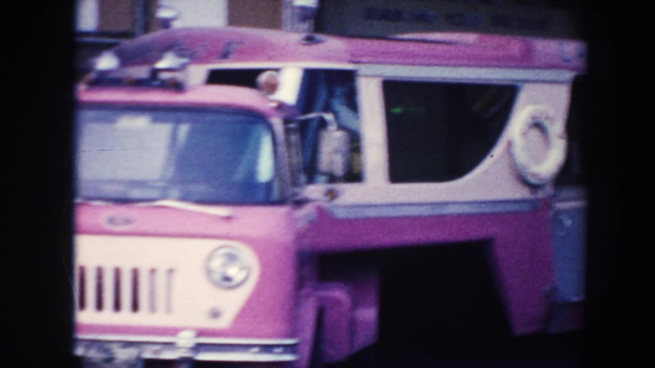 The pink and white bus appears in closer view, showing its front grille, side windows, and roof fittings.