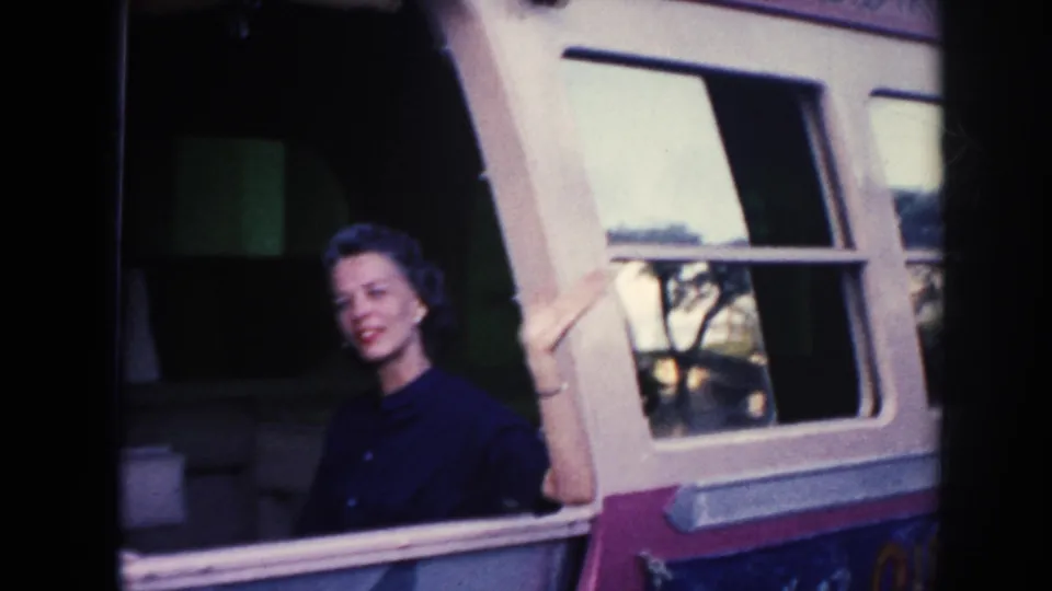A woman in dark clothing smiles from an open bus window in this 1961 Hawaii home-movie frame.
