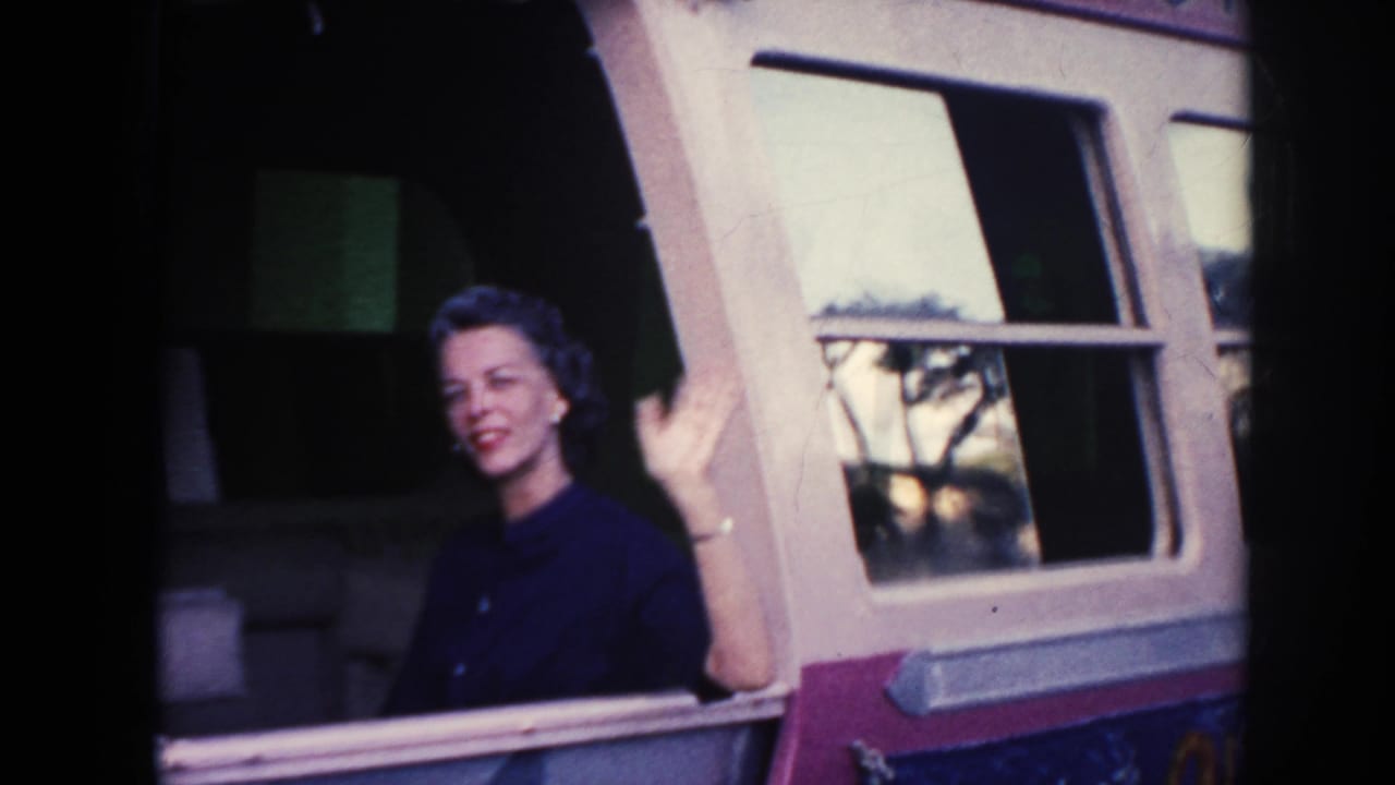 Woman in a dark dress waves from a ship window.