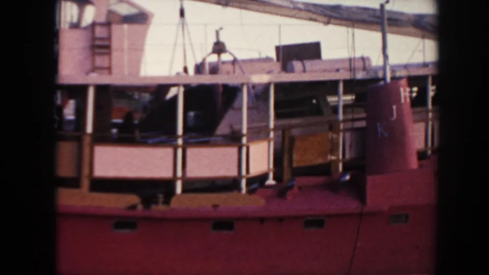 The docked vessel exterior shows railings, ladders, deck equipment, and the visible name marking Ala Kai II on the red hull.