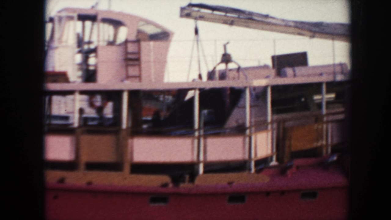 Red ship side with deckhouse, railings, rigging, and a crane behind it.