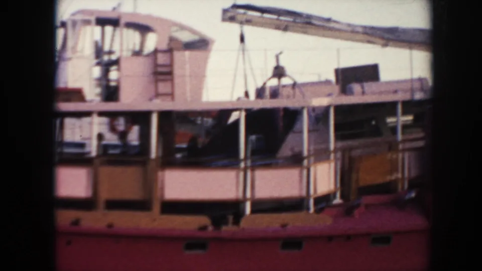 1961 Hawaii 8mm frame showing a red docked ship with pale deckhouse panels, railings, rigging, and harbor machinery behind it.