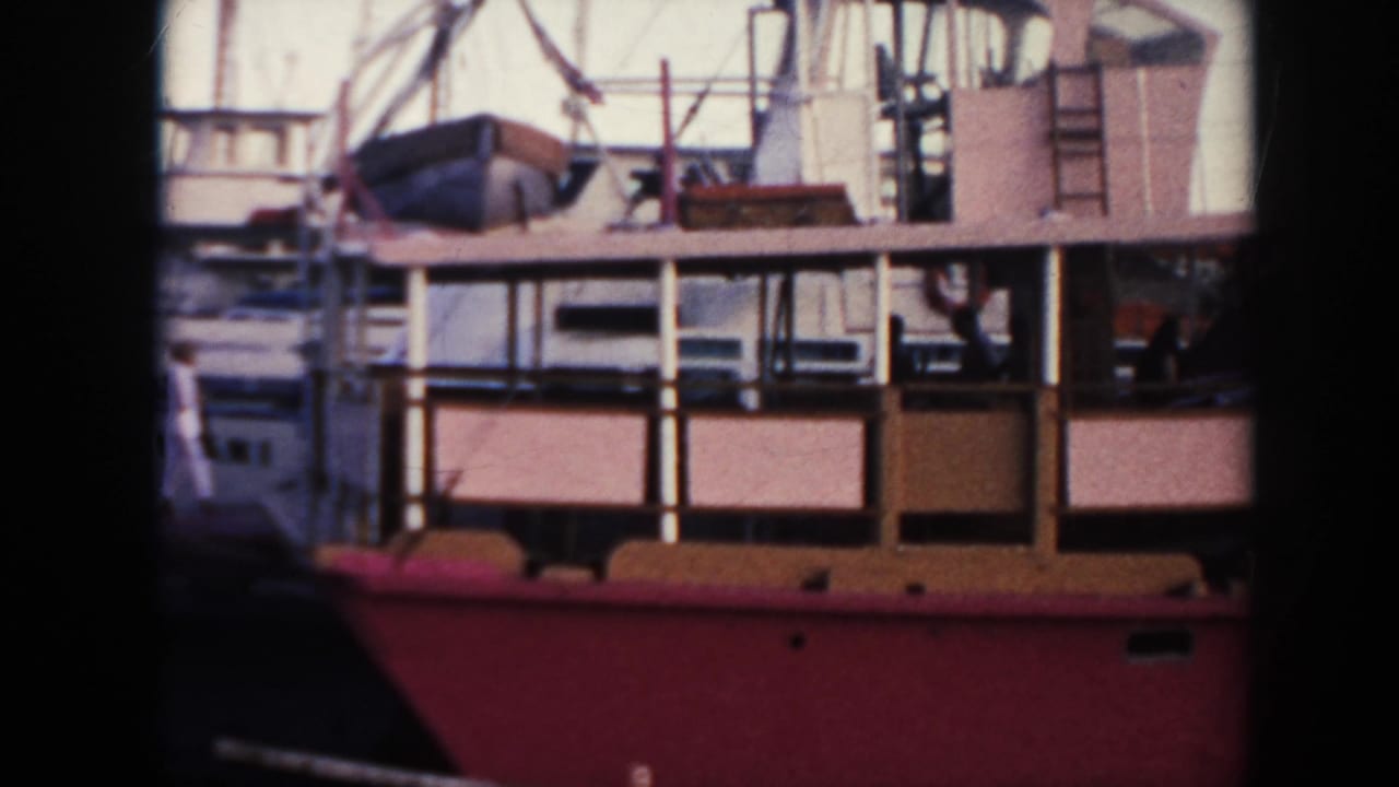 1961 Hawaii harbor view of the red vessel's midsection, with railings, cabin windows, rigging, and other boats close by.