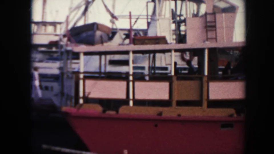 1961 Hawaii harbor view of the red vessel's midsection, with railings, cabin windows, rigging, and other boats close by.