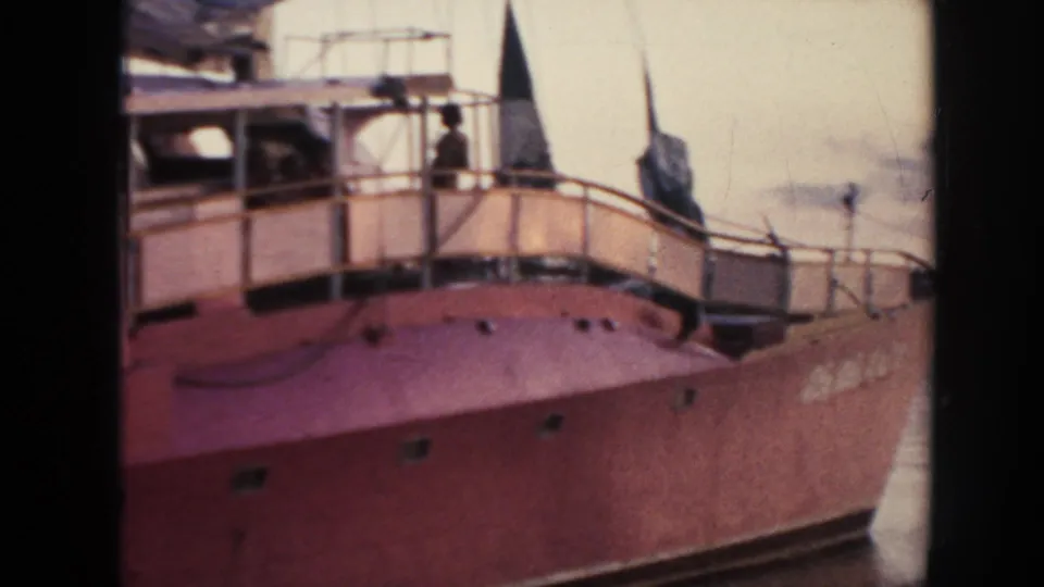 1961 Hawaii frame of the red ship's forward section, with curved railing, pale cabin structure, mast or flag shape, and water beyond.