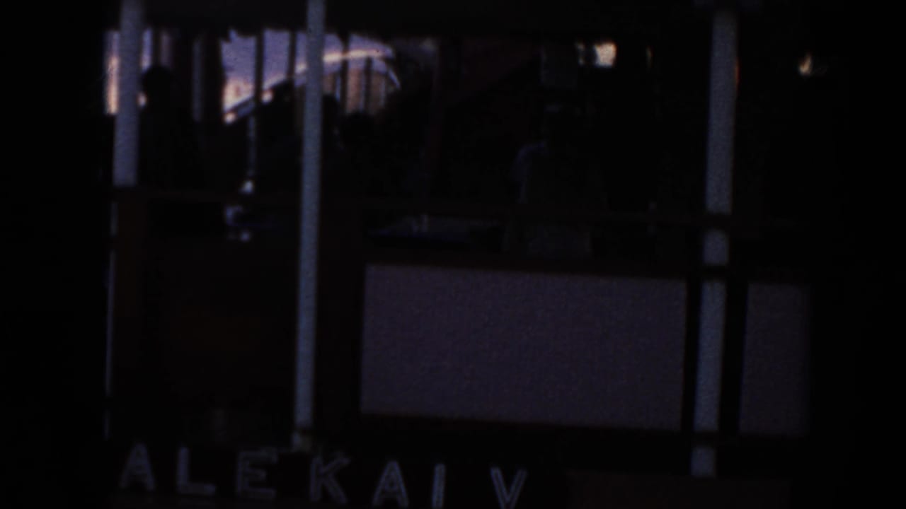 Dark 1961 Hawaii 8mm frame showing a docked boat area with partial Alekai V lettering and silhouetted railings.