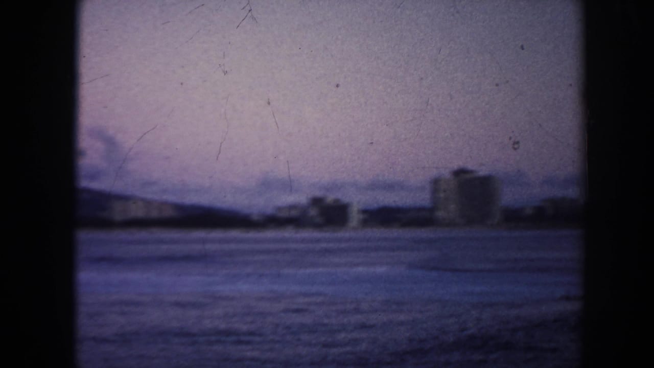 Soft 8mm view across water toward distant low buildings and a mountain ridge.