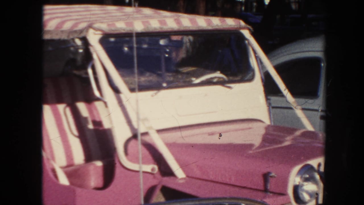 1961 Hawaii home-movie frame showing a pink-and-white open jeep with a striped canopy beside a light blue car.