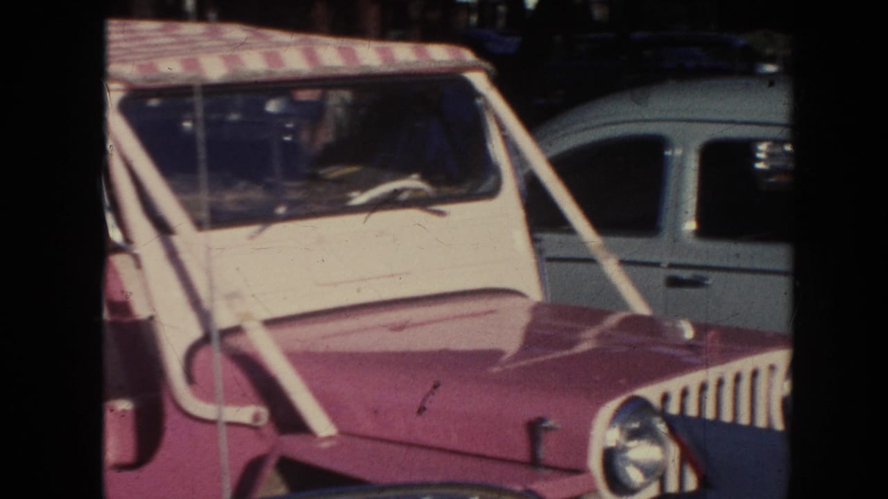 1961 Hawaii frame with the front of a pink-and-white jeep, striped canopy, windshield, and a light blue car nearby.