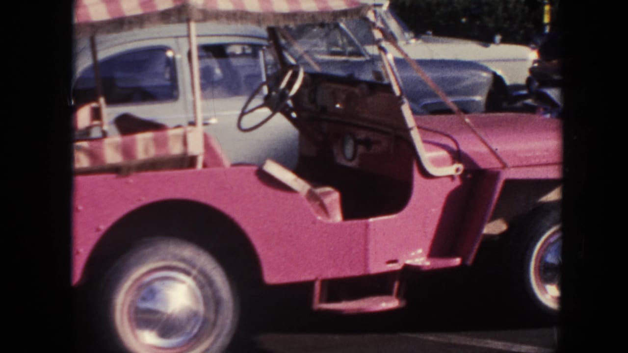 1961 Hawaii home-movie frame with a close side view of the pink buggy, open cabin, striped canopy, and front wheel.