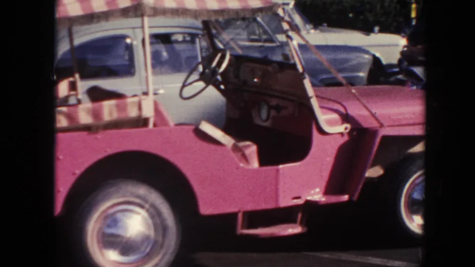 1961 Hawaii home-movie frame with a close side view of the pink buggy, open cabin, striped canopy, and front wheel.
