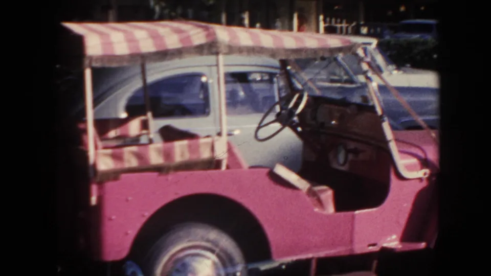 1961 Hawaii 8mm frame showing the open buggy in side view, with its striped canopy and several parked cars behind it.