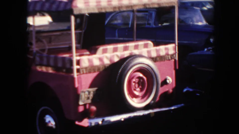 1961 Hawaii frame showing the rear of the pink open buggy, including striped bench seating, canopy posts, and a rear-mounted spare tire.