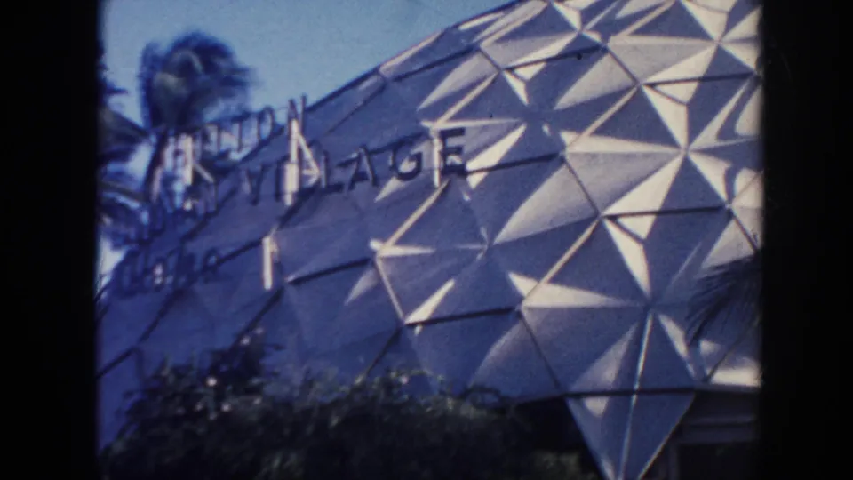1961 Hawaii frame with partial Hilton Hawaiian Village signage across a geometric dome facade beside palm trees.