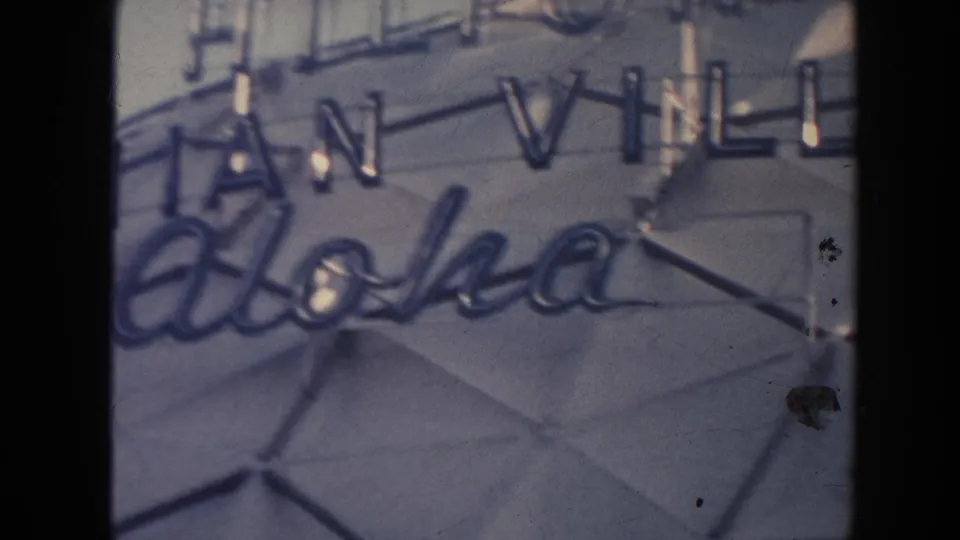 1961 Hawaii home-movie frame with Aloha script and partial Hilton Hawaiian Village letters on a gray facade.