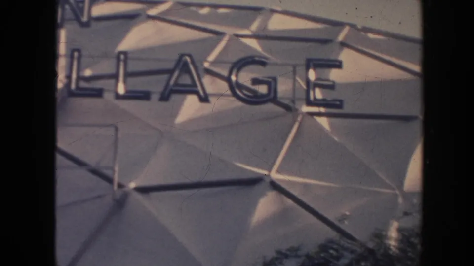 1961 Hawaii 8mm frame showing partial Village sign lettering over a faceted gray hotel facade.