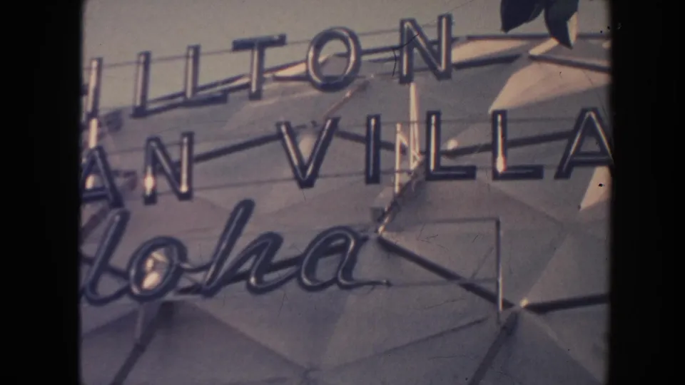 1961 Hawaii 8mm frame showing a close view of Hilton Hawaiian Village signage and Aloha lettering on a hotel exterior.