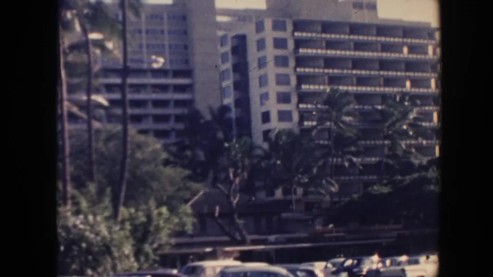 1961 Hawaii 8mm frame showing a Hilton Hawaiian Village hotel tower with balconies, windows, palms, and landscaping.