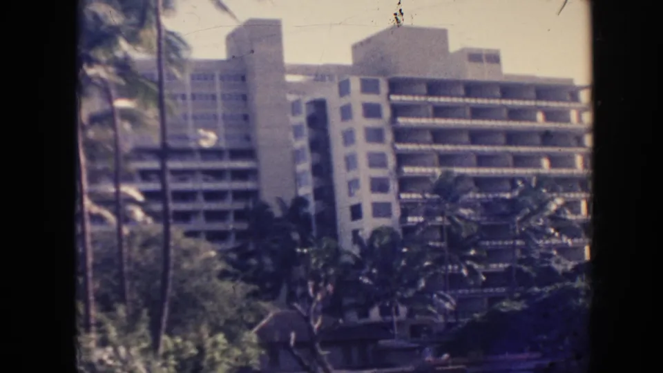 1961 Hawaii 8mm frame with hotel balconies, palm trees, landscaping, and dark film-edge borders from the scanned reel.