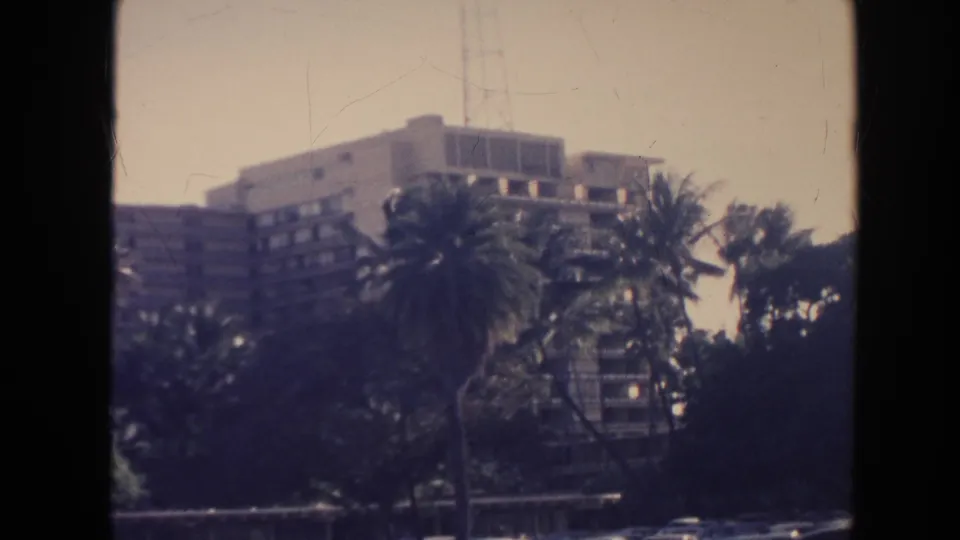 1961 Hawaii home-movie view of tall palms and shadowed trees in front of a large mid-century building.
