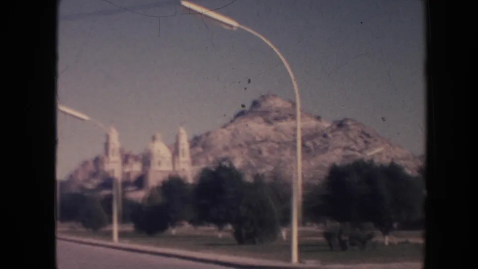 Soft 1961 Hawaii 8mm frame showing the mountain and distant church-like structure through roadside trees and a prominent curved streetlight.
