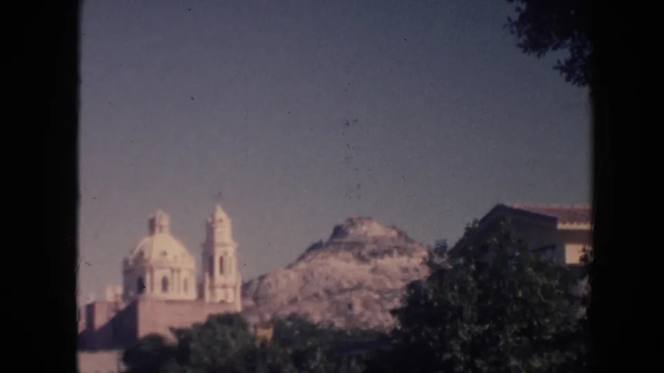 1961 Hawaii frame with a distant church-like building, rocky mountain, dark foreground tree, and partial roofline at the right edge.
