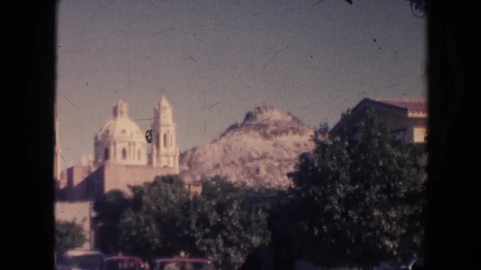 Distant Hawaii landmark view on 8mm film, showing domes and towers above trees with hillside and parked cars partly visible.