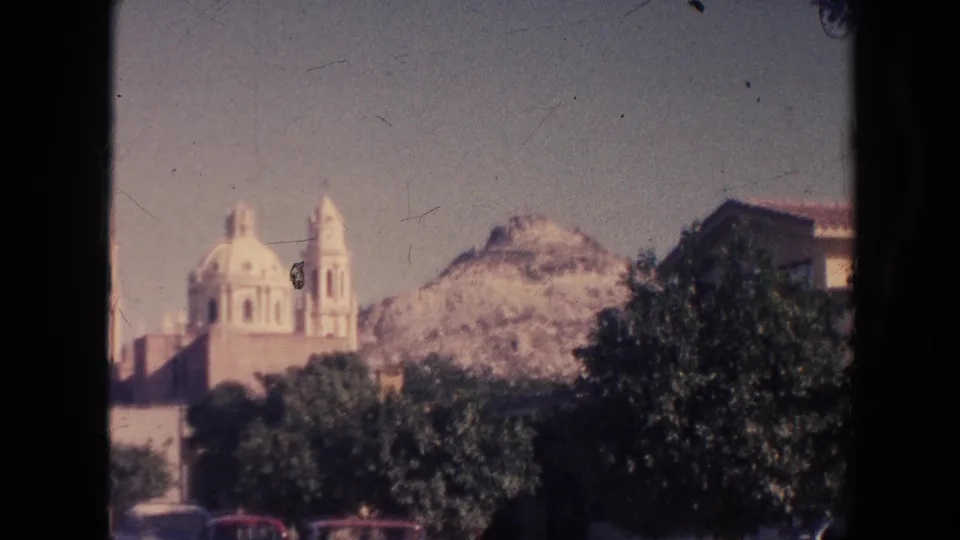 1961 home-movie still showing a distant church-like structure in Hawaii, softened by 8mm focus and framed by trees and hillside.
