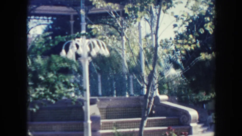 Hawaii 1961 home-movie view of a landscaped courtyard with trees, stepped seating, concrete edging, and a white decorative lamppost.