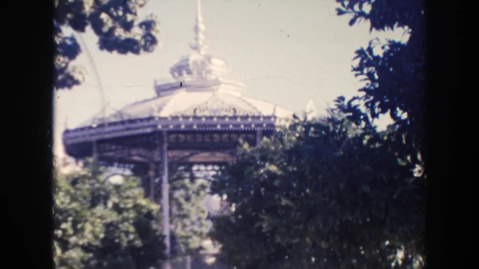 1961 Hawaii park view of a domed gazebo and open pavilion structure partially hidden by dark foreground foliage.