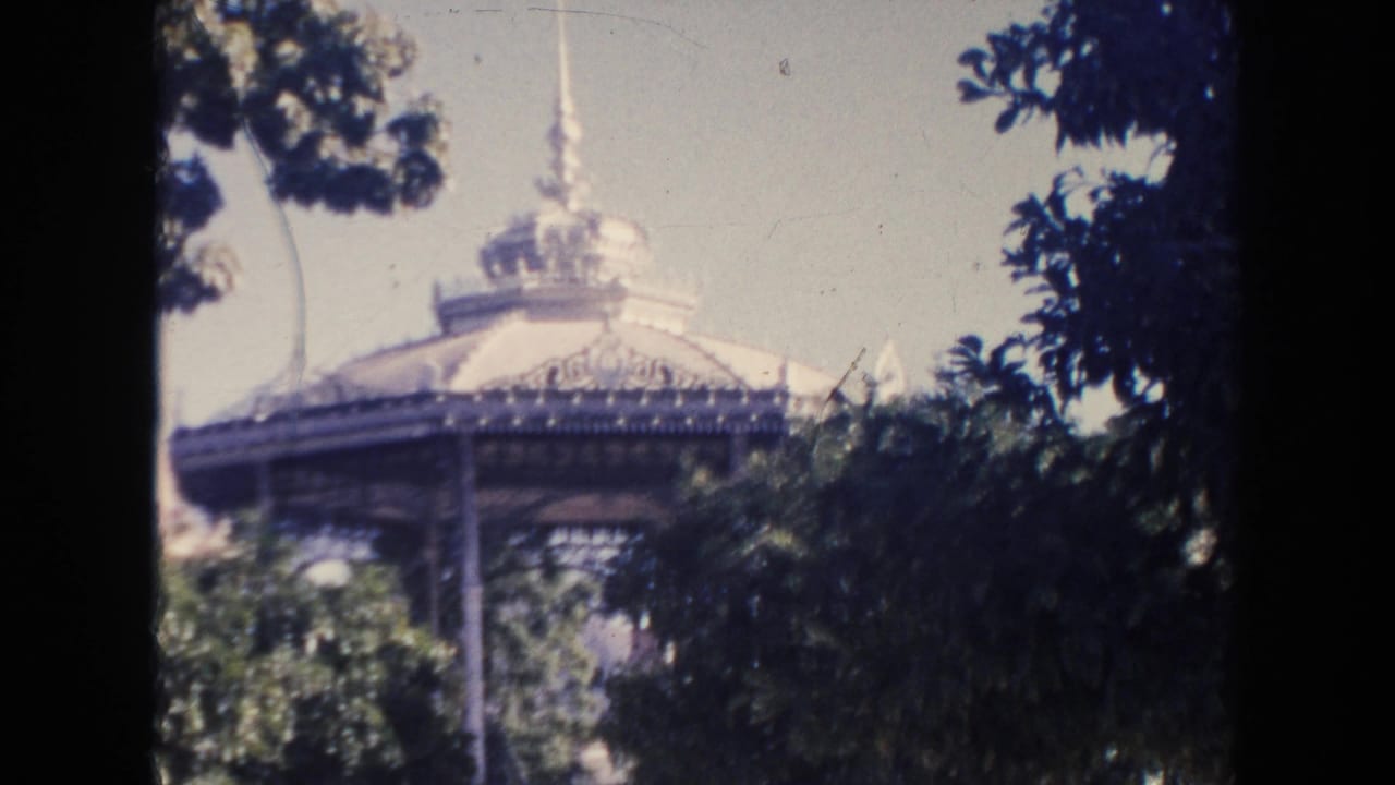 Ornate domed gazebo partly hidden by trees in a sunlit park.