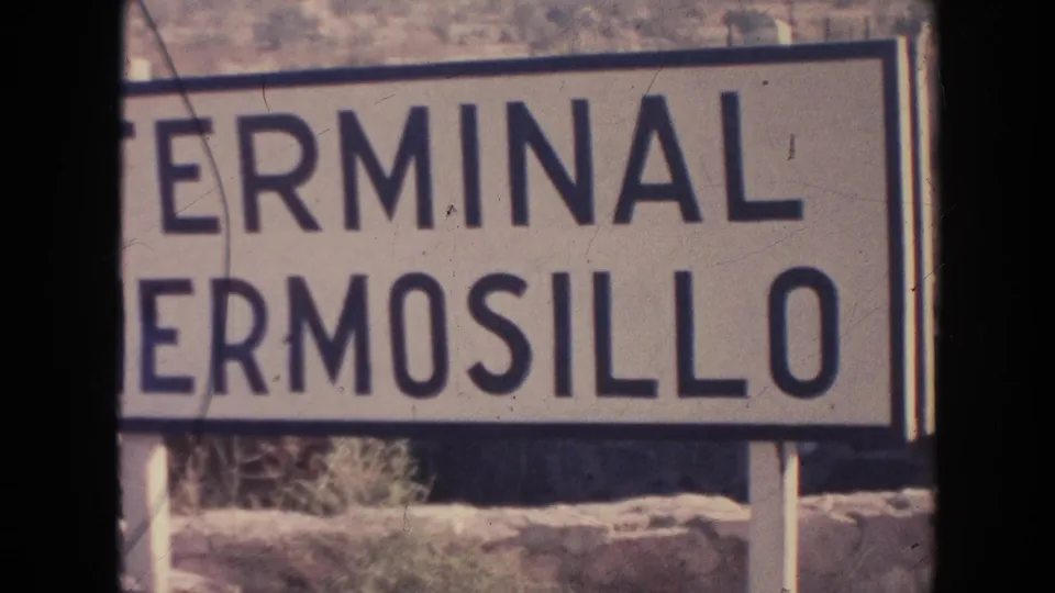 1961 8mm frame with a white Terminal Hermosillo sign filling the right side, backed by a dry hillside and film gate edges.