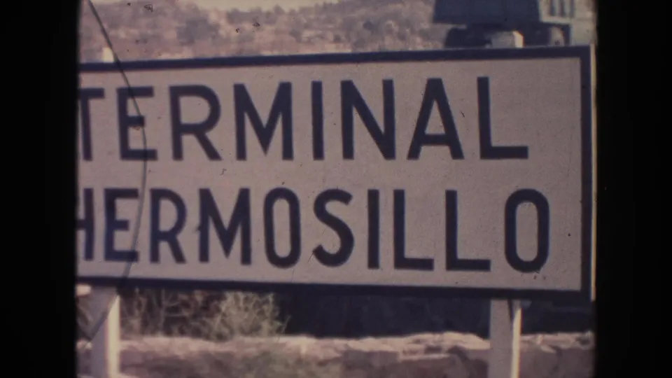 Close 1961 8mm view of the Terminal Hermosillo sign, cropped at the left edge with posts and hillside visible behind it.