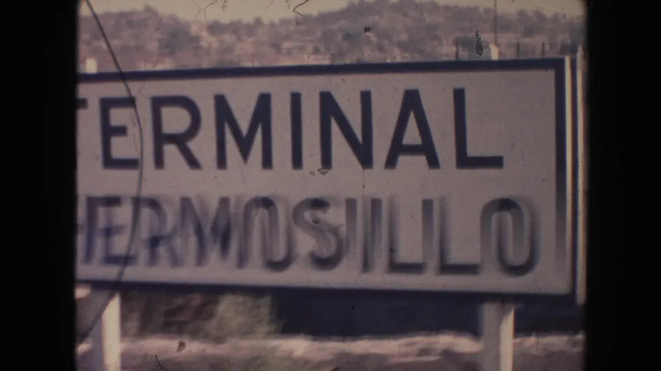 Final 1961 8mm frame shows the Terminal Hermosillo sign blurred by camera movement, with hillside, posts, and film artifacts visible.