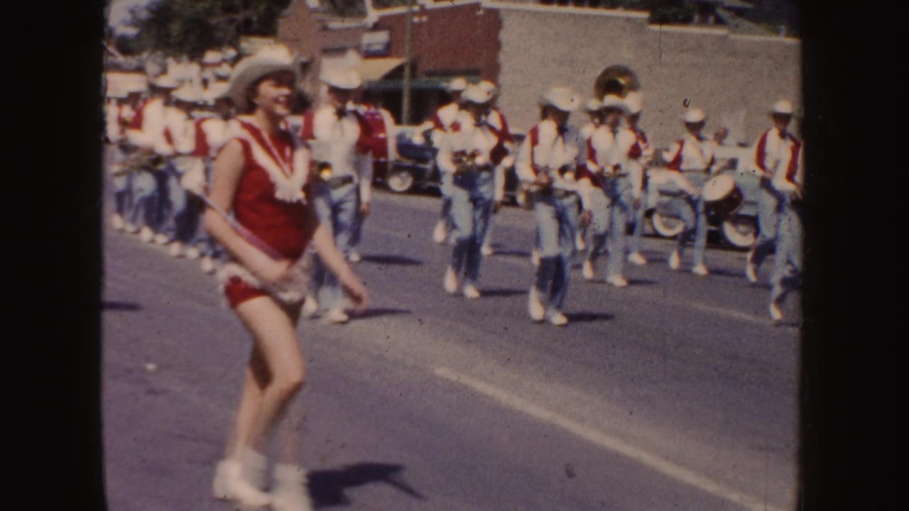 Red-and-white parade performer passes in front of a marching band in cowboy hats.
