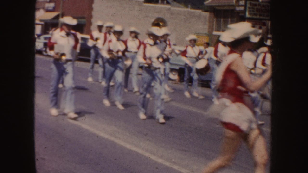 Marching band members in cowboy hats move down the street with drums and brass.