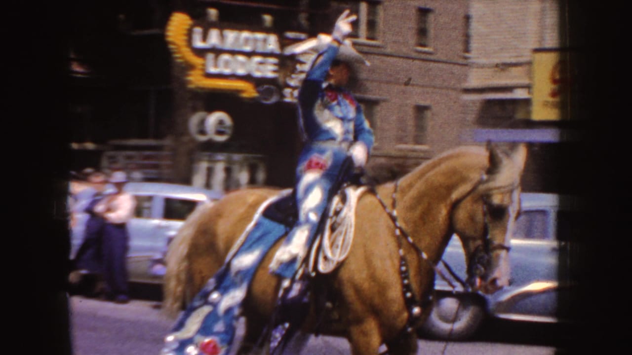 Woman in a Western riding outfit waves from a palomino horse during a town parade.
