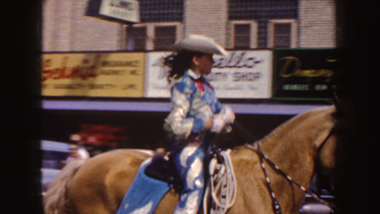 Mounted woman in a cowboy hat rides past storefront signs during the parade.