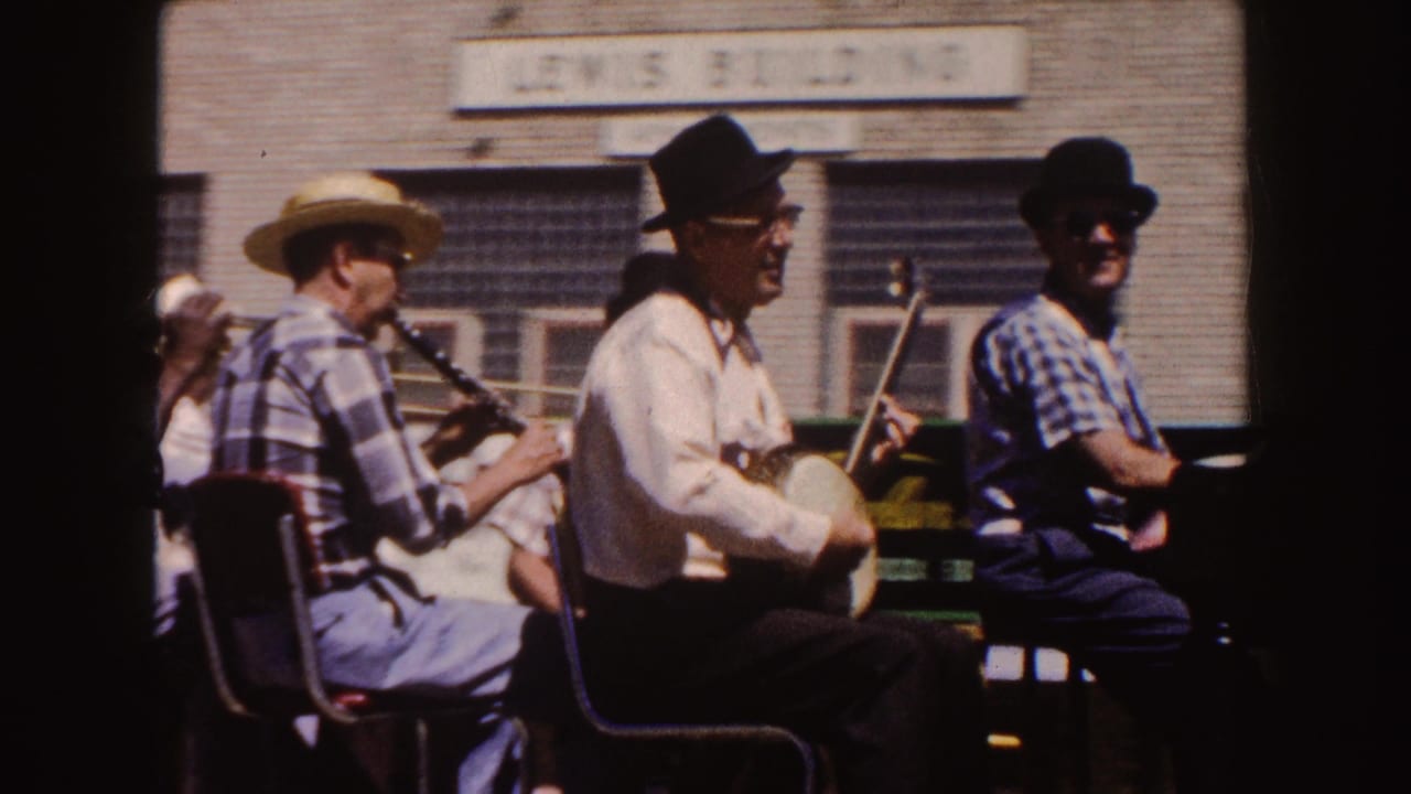 Outdoor folk musicians sit near a brick building, including a banjo player and a clarinet player, with signage above them.