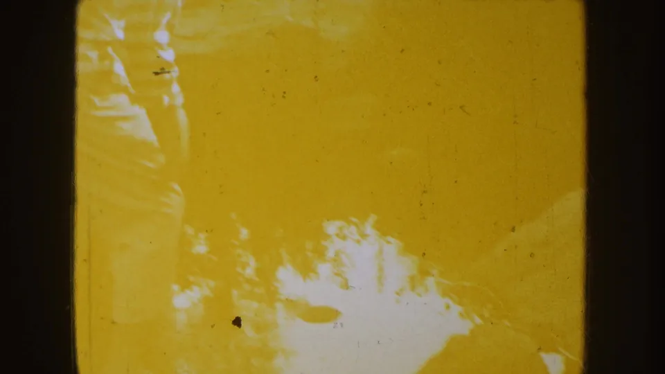 Yellow-tinted 8mm frame with faint tree or sky shapes and visible dust, scratches, and exposure variation.